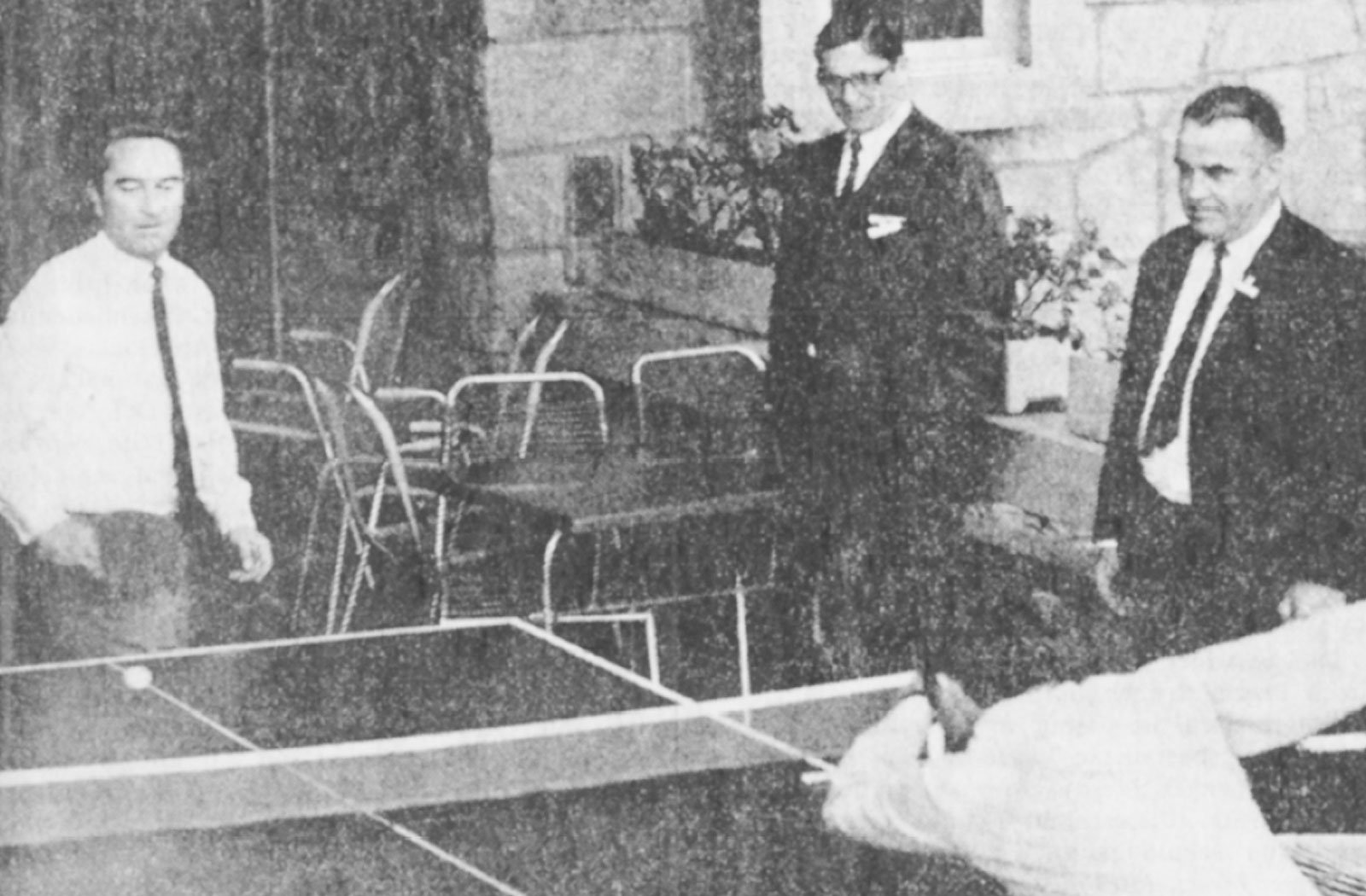 Due uomini giocano a ping pong sotto lo sguardo divertito di altri due.