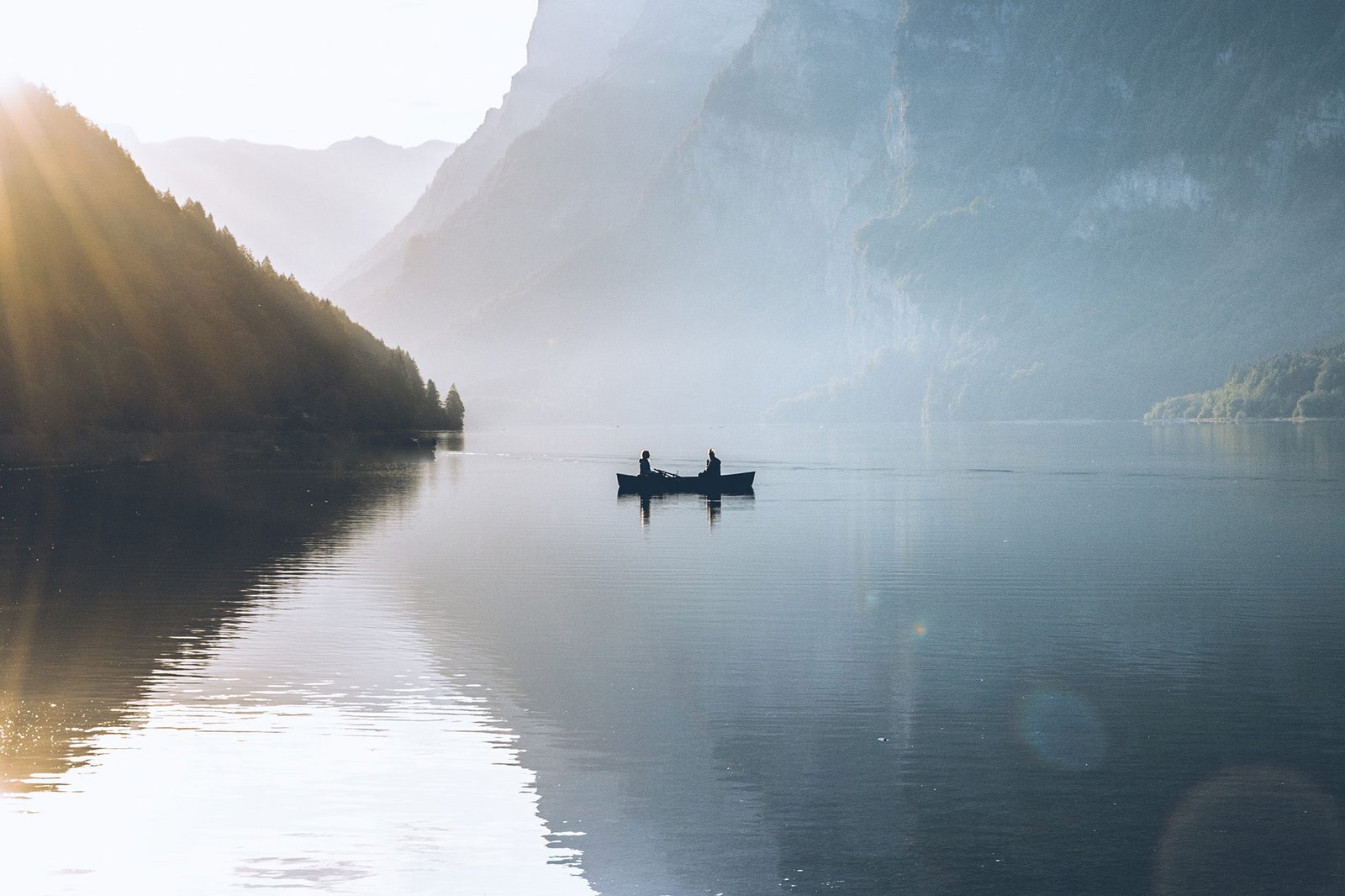 Deux personnes sont sur une petite barque au milieu d'un lac. Le soleil couchant commence à disparaître derrière les montagnes avoisinantes.